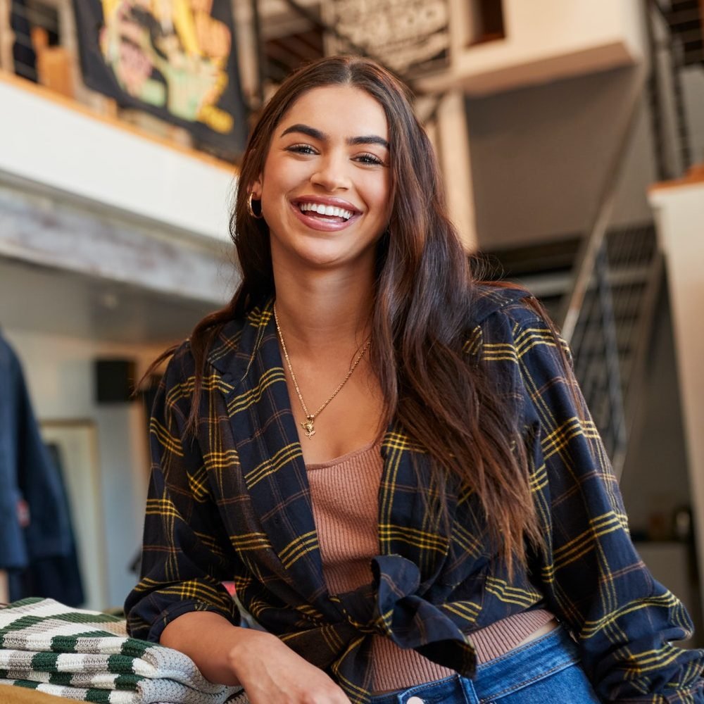 Portrait Of Smiling Female Owner Of Fashion Store Standing In Front Of Clothing Display